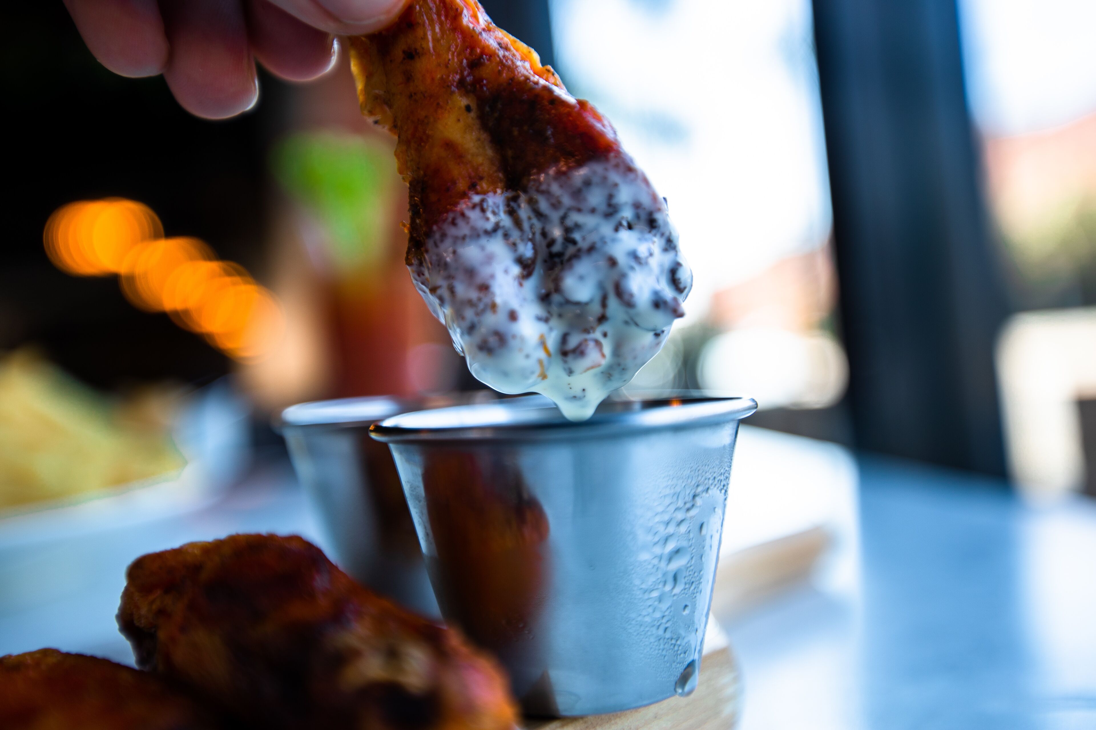 A hand dipping a piece of food into a metal cup.