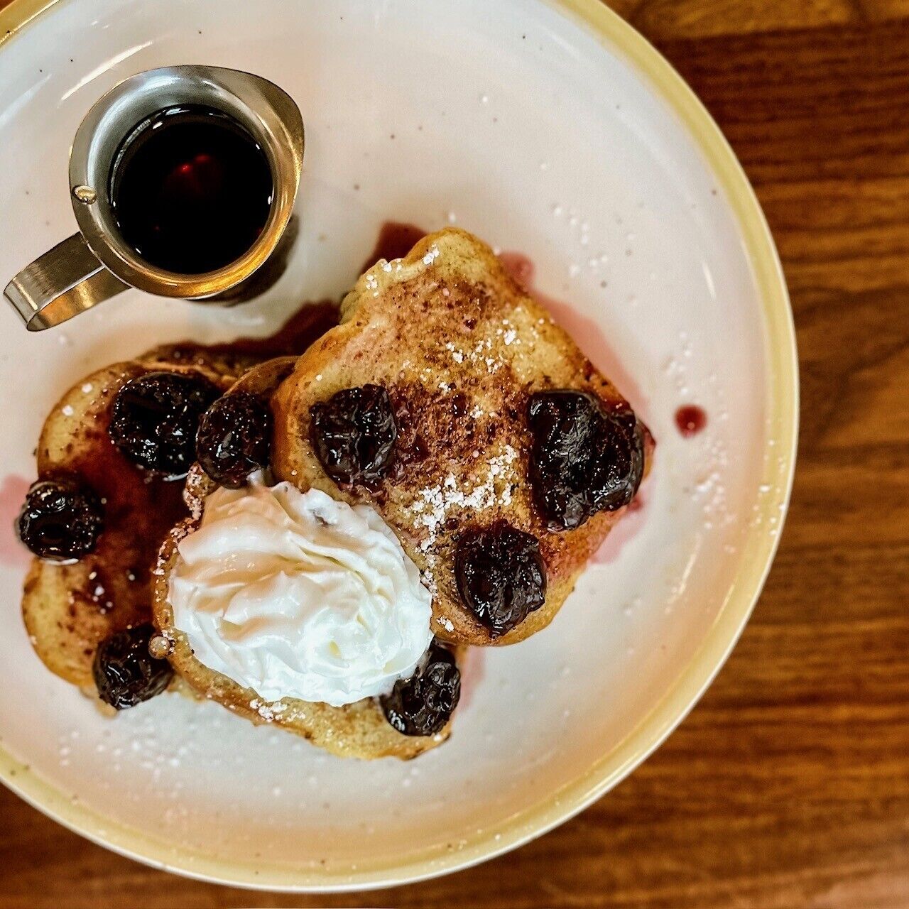 A plate with pancakes topped with syrup, blueberries, and a dollop of whipped cream.