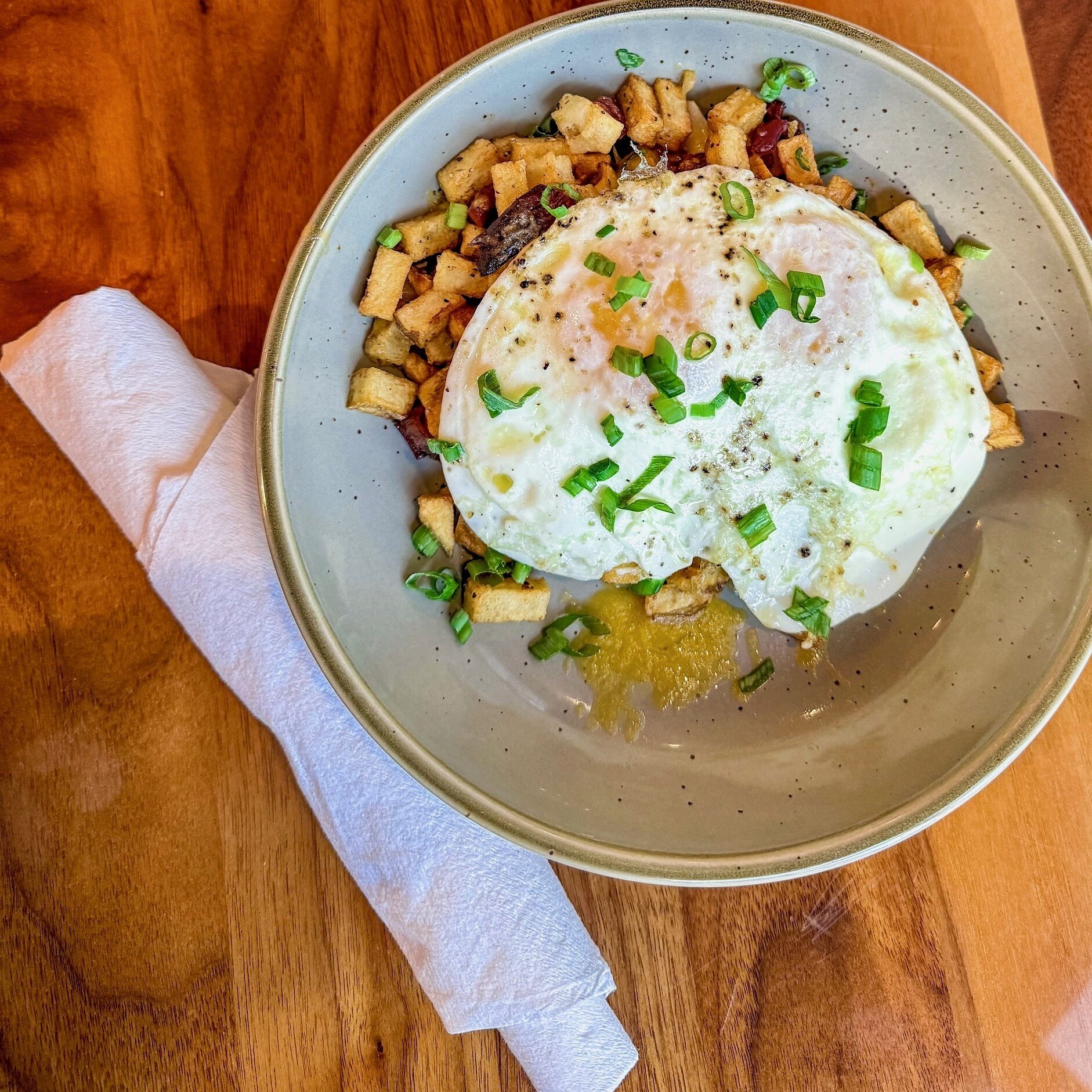 A plate with a fried egg, diced potatoes, and green onions on a ceramic plate.