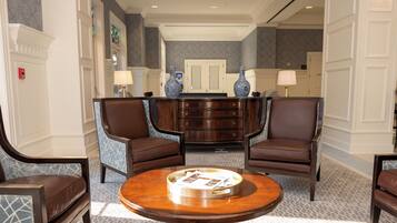 Un vestíbulo con una mesa de madera central, dos sillones de cuero marrón, un sofá azul estampado y un jarrón decorativo.