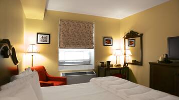 Una habitación de hotel con una cama, una silla roja, un escritorio con lámpara y una ventana con persiana de hojas.