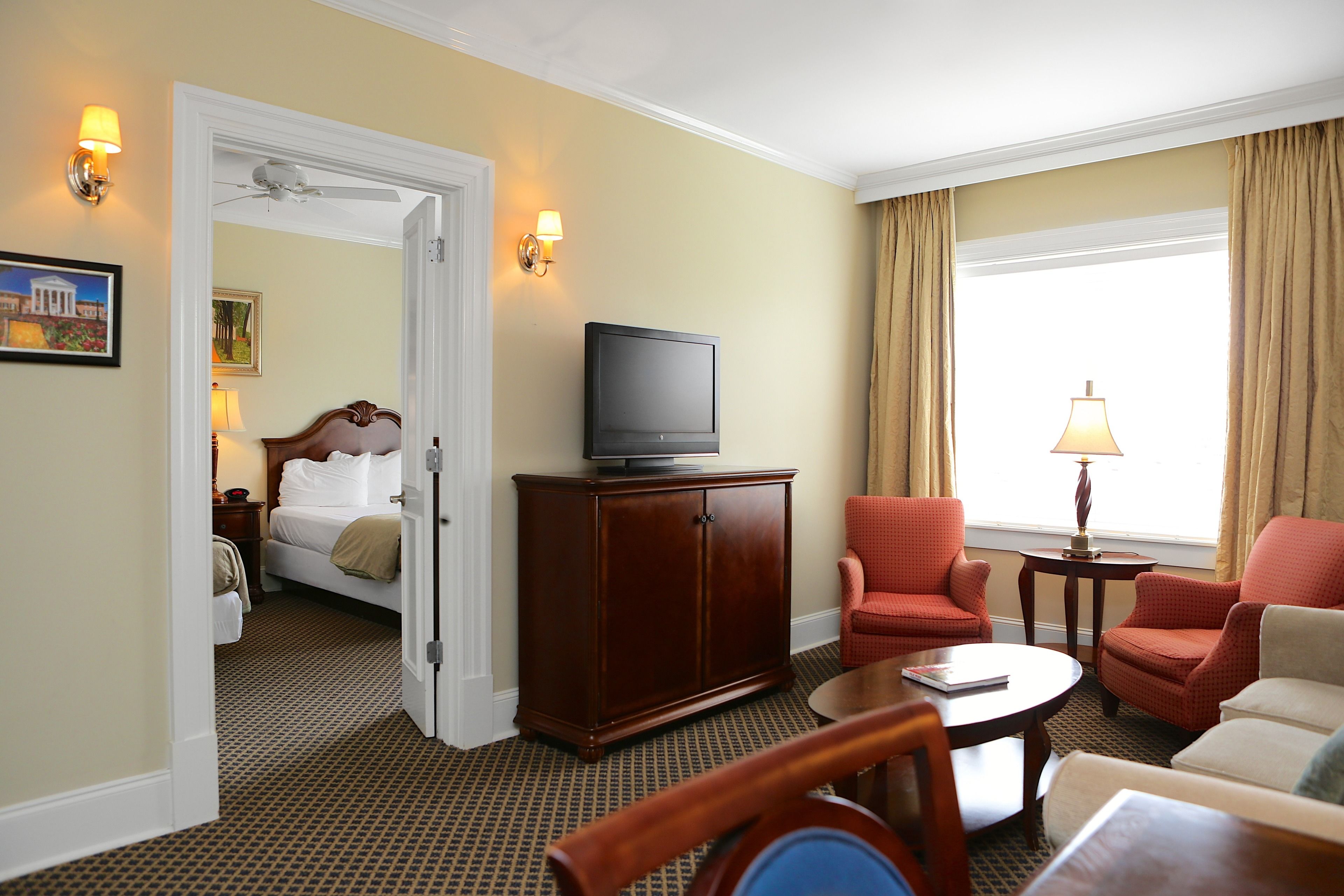 A hotel room with a bed, a television on a wooden cabinet, two armchairs, a coffee table, and a lamp.