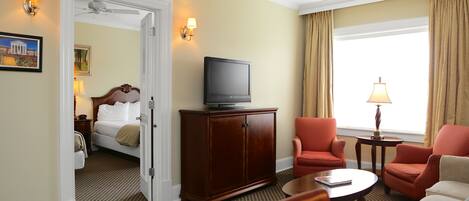 A hotel room with a bed, a television on a wooden cabinet, two armchairs, a coffee table, and a lamp.