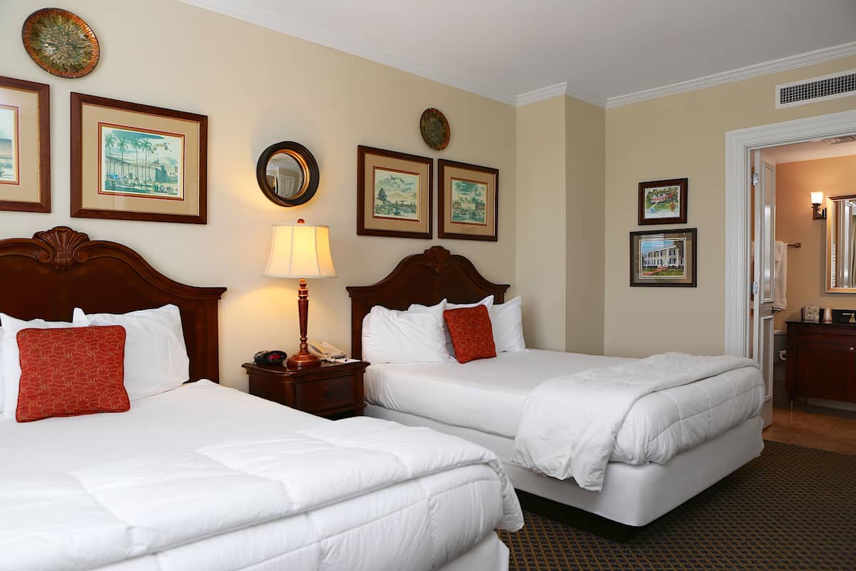 A hotel room with two beds, a nightstand with a lamp, and framed pictures on the wall.