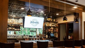 A bar area with a large screen displaying "The Inn McCormick's Aloe Mint" logo, wooden bar counter with bottles, and seating area with tables and chairs. - The Inn at Ole Miss (University)