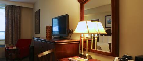 Ein Hotelzimmer mit Fernseher, Schreibtisch mit Lampe, Stuhl und Spiegel.