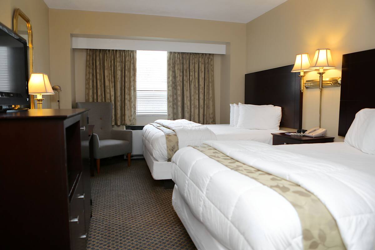 A hotel room with two beds, a desk, a chair, a TV, and a lamp.