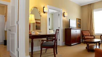 A hotel room with a desk, chair, television, and a cabinet.