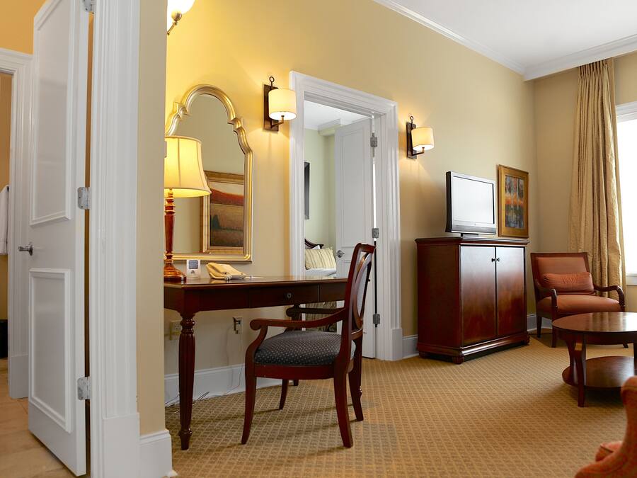 A hotel room with a desk, chair, television, and a cabinet.