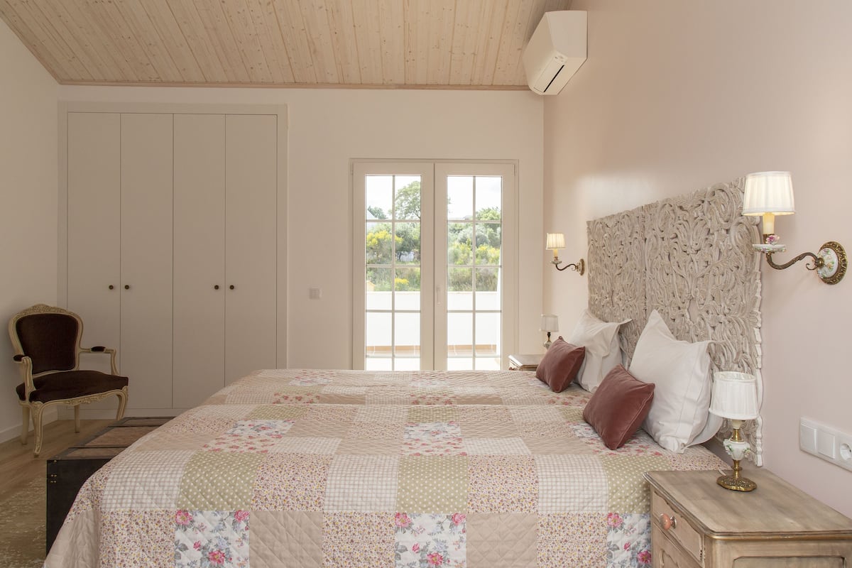 A bedroom with a large bed, a chair, a dresser, and a window with a view of greenery.