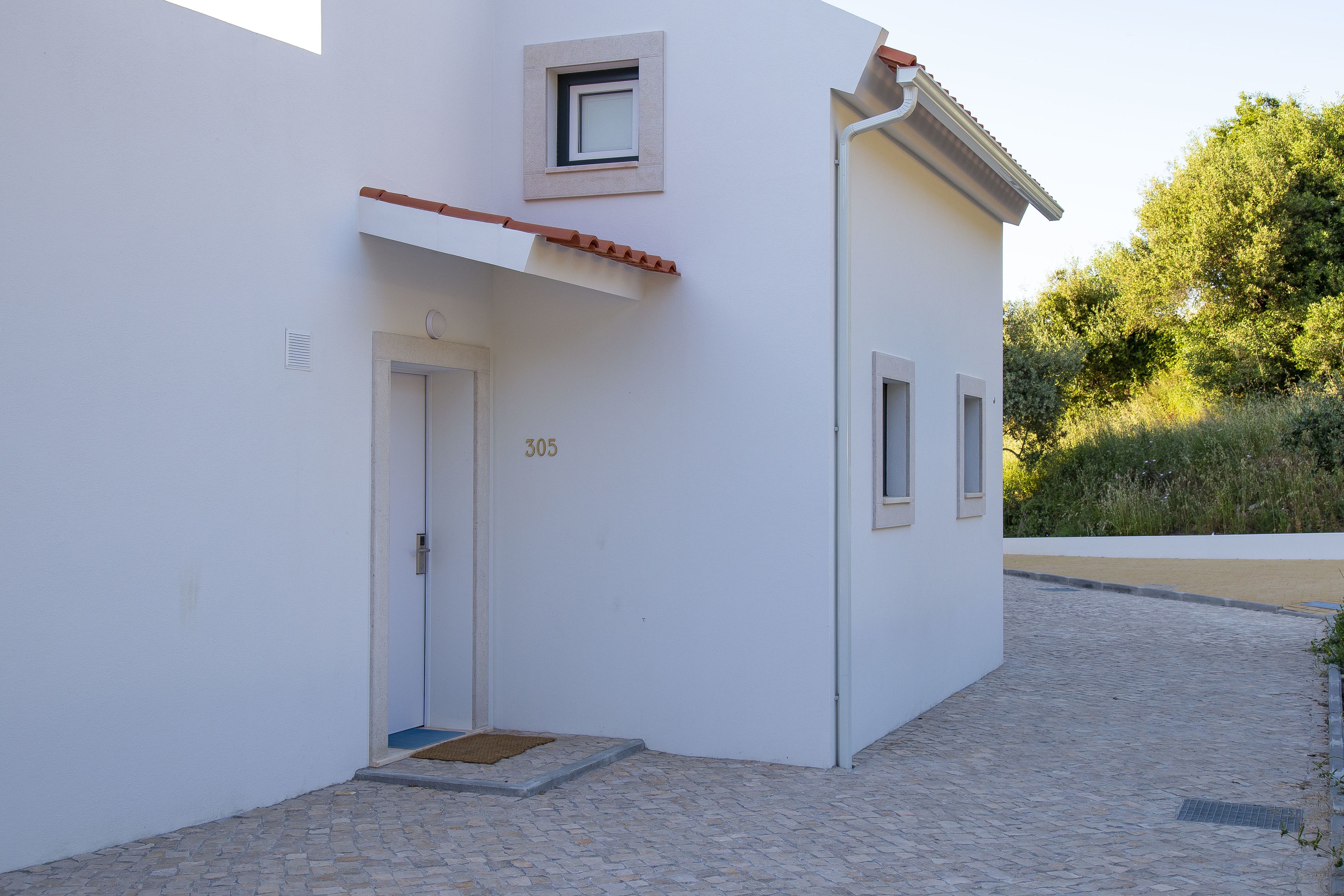 Un bâtiment moderne à la façade blanche, avec le numéro « 305 » sur la porte et une petite fenêtre au-dessus de la porte.
