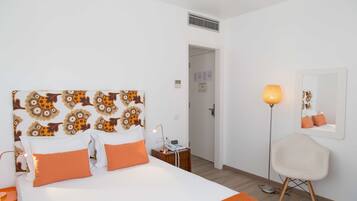 Habitación de hotel con cabecera estampada, mesita de noche con lámpara, una silla y un espejo en la pared.