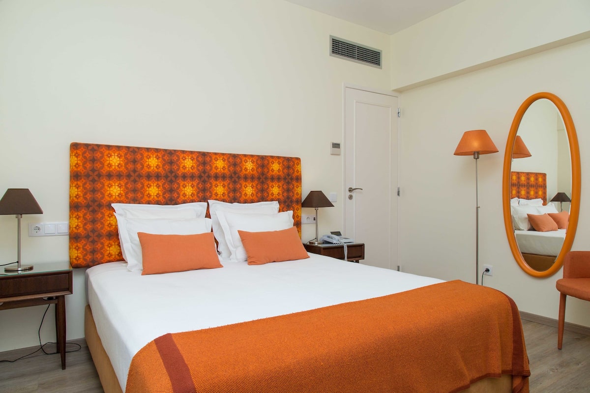 A hotel room with a large bed, two bedside tables, a mirror, and a chair.
