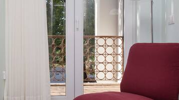 Habitación con una silla roja, una lámpara de pie y vistas a un espacio exterior con barandilla de metal y vegetación a través de una puerta de cristal.