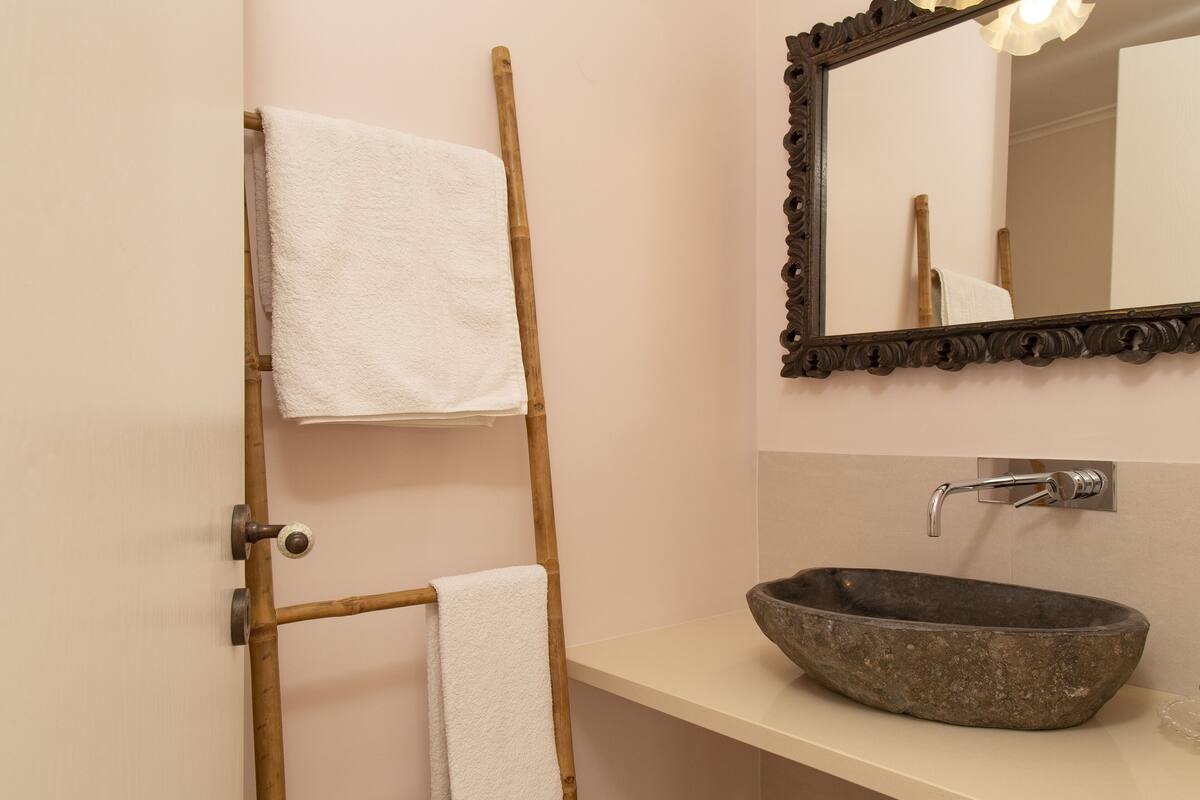 A bathroom with a bamboo towel rack, a stone sink, and a mirror with an ornate frame.