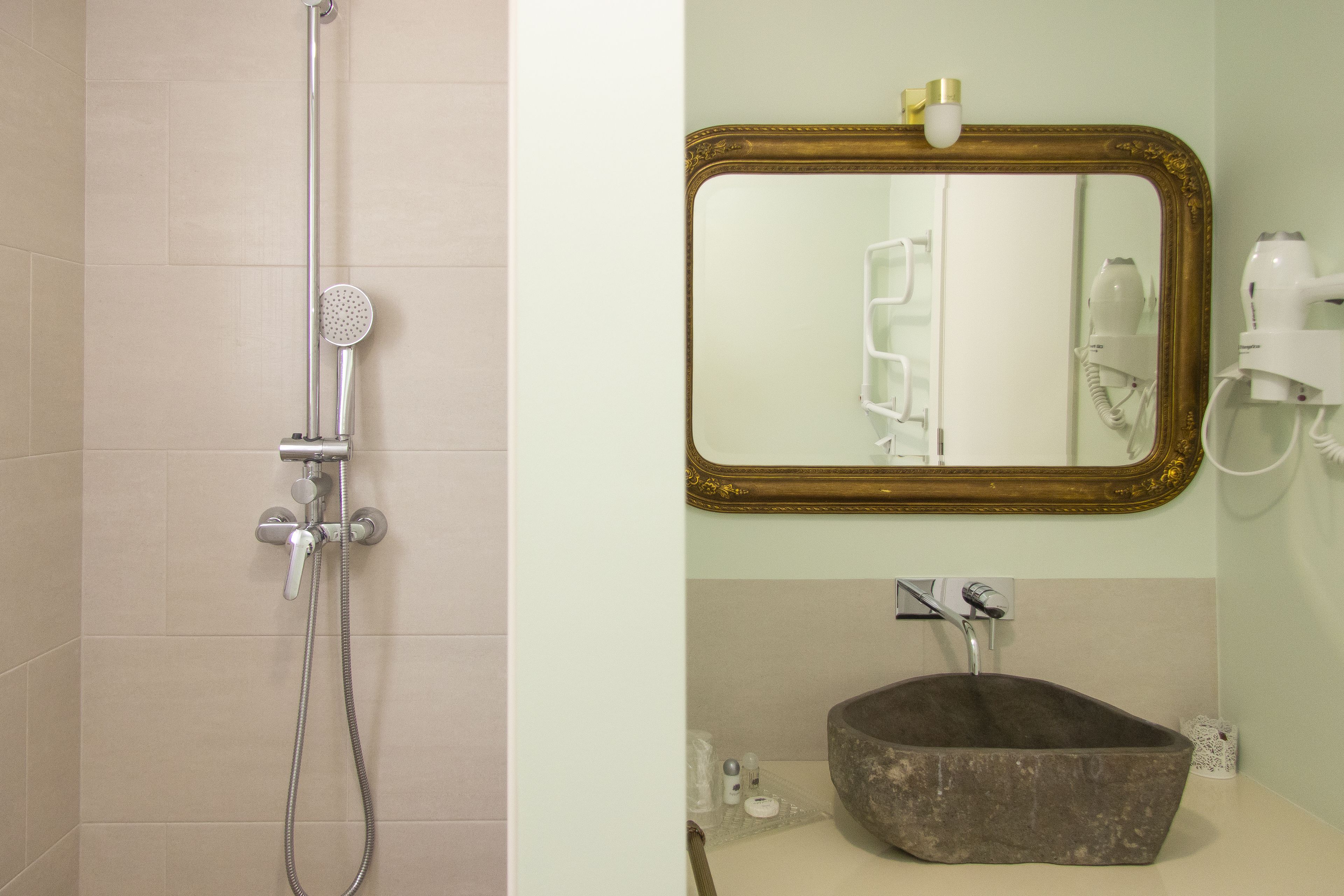 Ein Badezimmer mit Dusche, Waschbecken mit großer Schale und Spiegel mit goldener Rahmung.