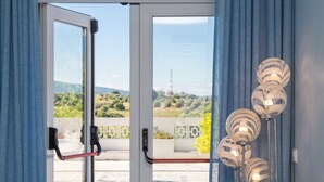 A room with a sliding glass door leading to an outdoor area with a view of greenery and a distant tower. There are three spherical light fixtures on the right side of the image. - Aires da Serra Hotel (Torres Novas)