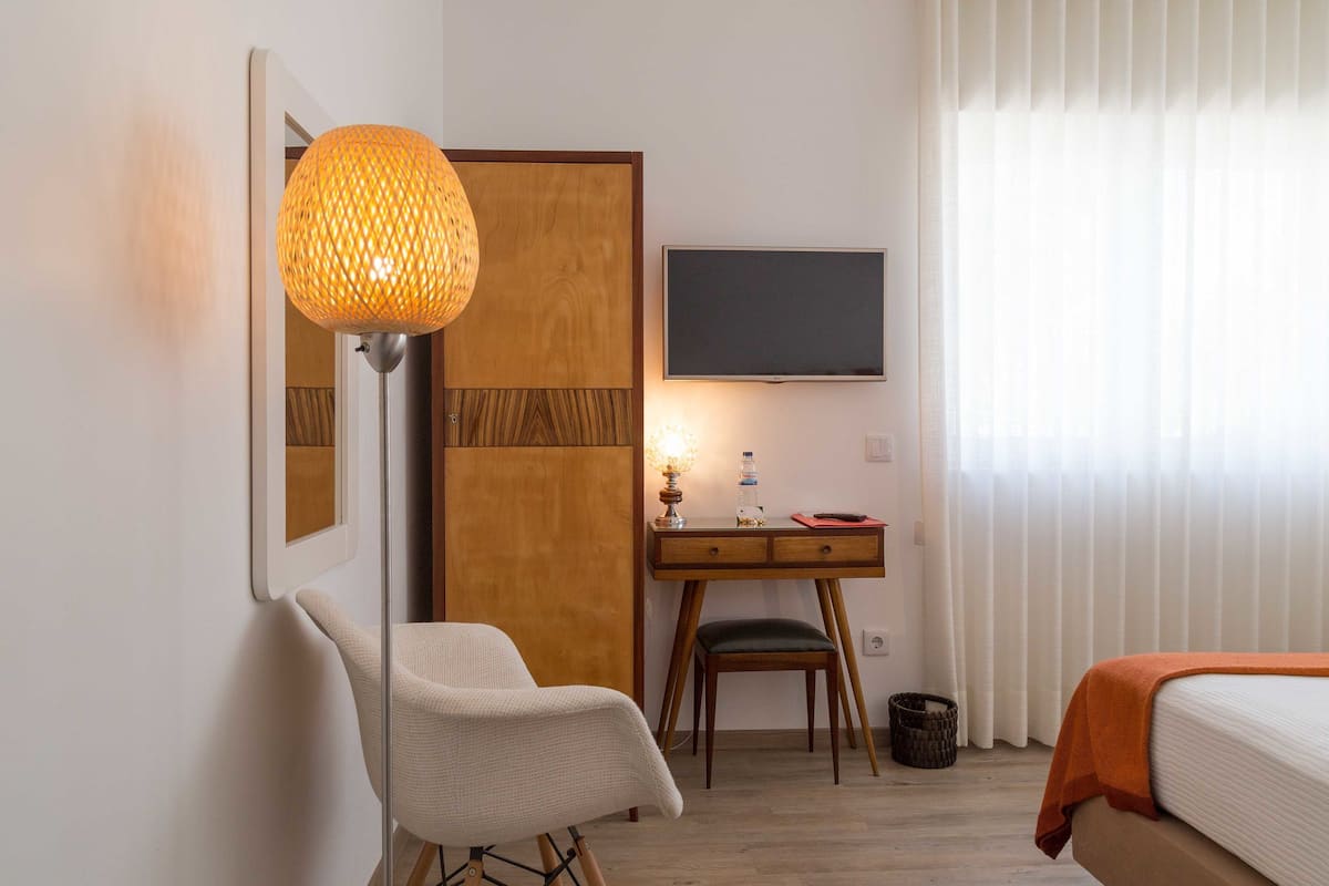 A hotel room with a bed, a desk with a chair, a lamp, and a TV on the wall.