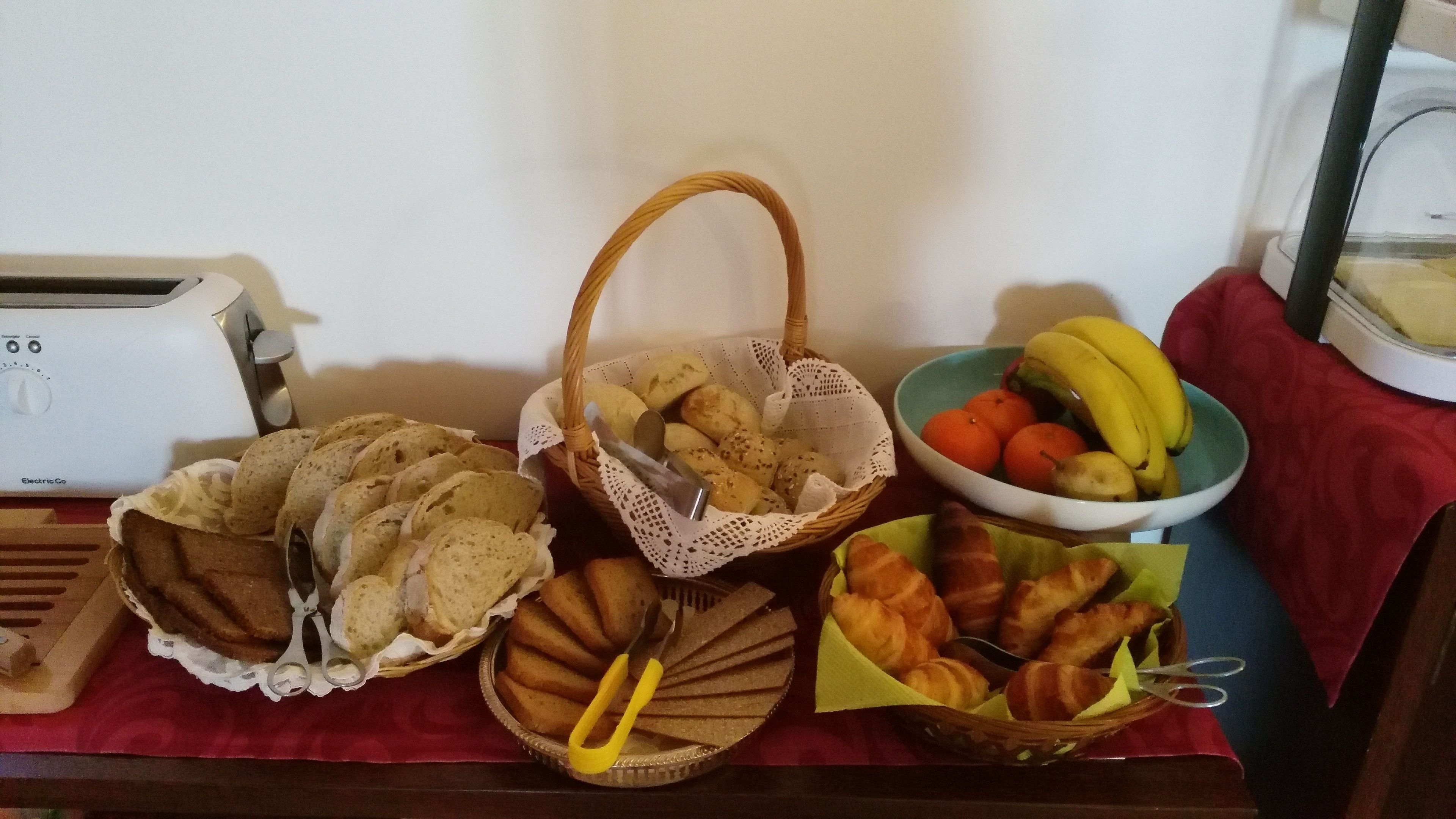 Een tafel met diverse etenswaren, zoals brood, gebak en een schaal fruit.