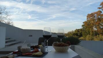 A table set with two wine glasses, a basket of bread, and a cheese board with various accompaniments.