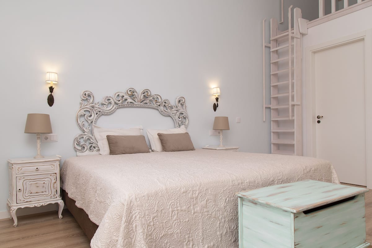 A bedroom with a bed, two bedside tables, a dresser, and a ladder leading to a closet.