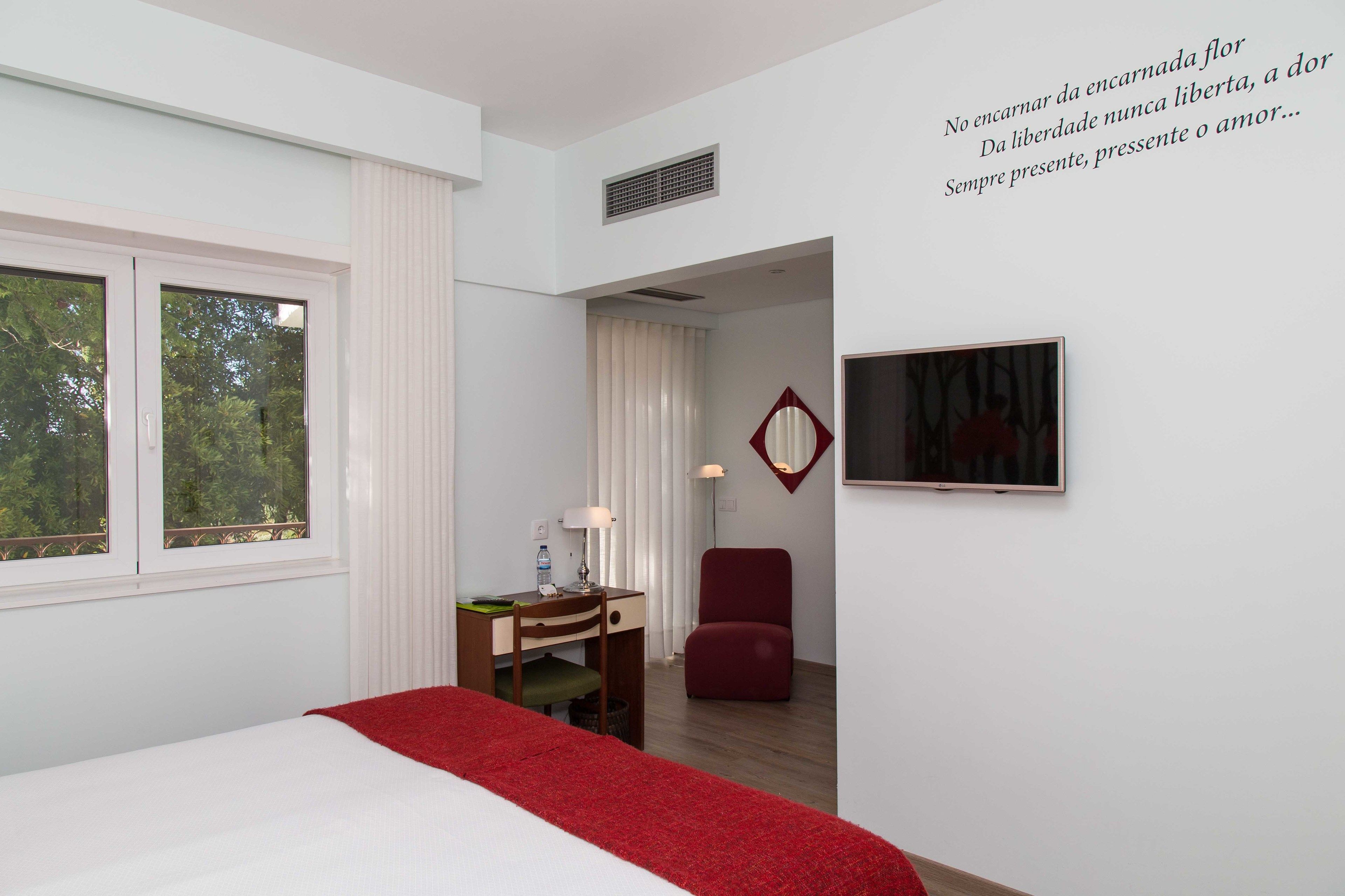 Habitación de hotel con cama, escritorio, silla, televisor y ventana con vista a árboles.