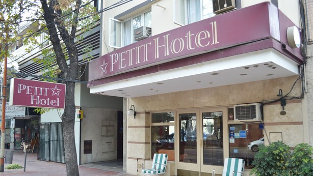 Ein Hotel Eingang mit einem Schild, auf dem 'PETIT Hotel' steht, und zwei Liegestühle davor.