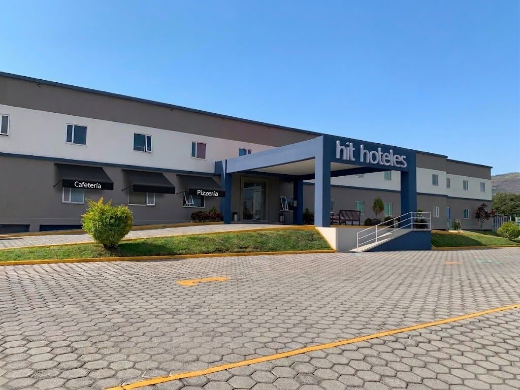 Entrada de hotel con un área techada que dice 'hit hotels', una cafetería y una pizzería.