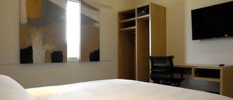 Un dormitorio con cama, escritorio, silla, armario y televisor montado en la pared.