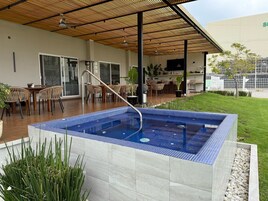 A modern outdoor pool area with a tiled deck, a covered seating area, and a view of the surrounding landscape.