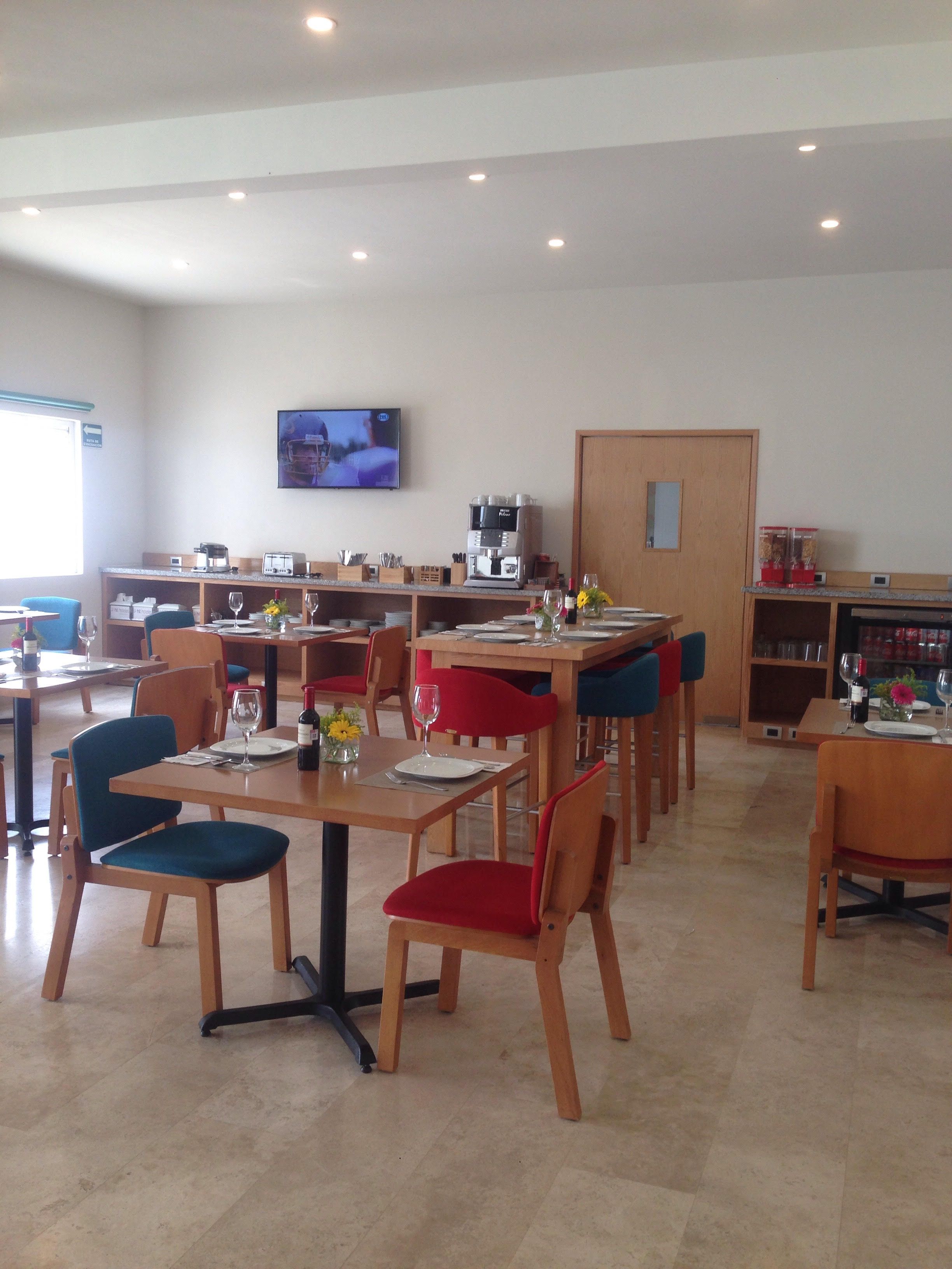 A dining area with multiple tables and chairs, a coffee machine, and a television mounted on the wall.