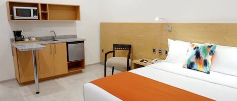 A hotel room with a bed, a desk with a microwave, a coffee maker, and a chair.