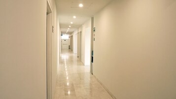 A long, narrow hotel corridor with a polished floor, white walls, and doors on both sides.