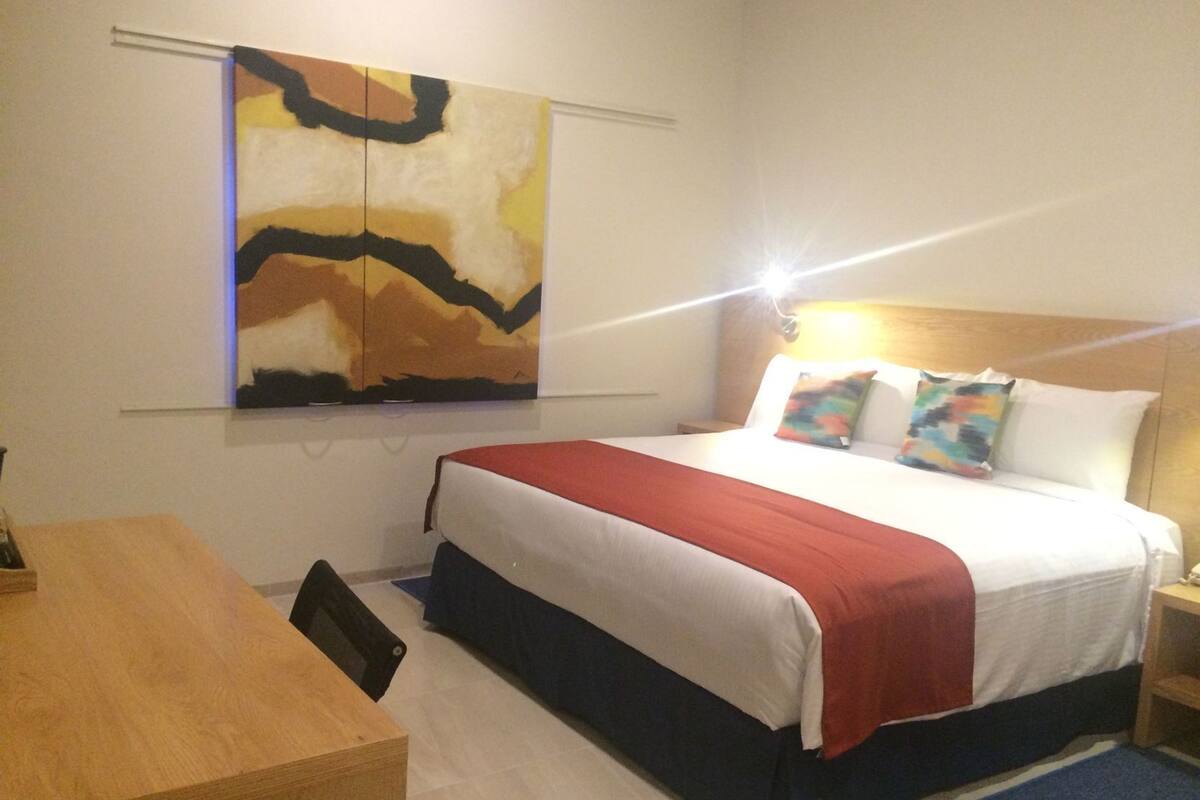 Une chambre d’hôtel avec un lit, un bureau et un grand tableau abstrait accroché au mur.