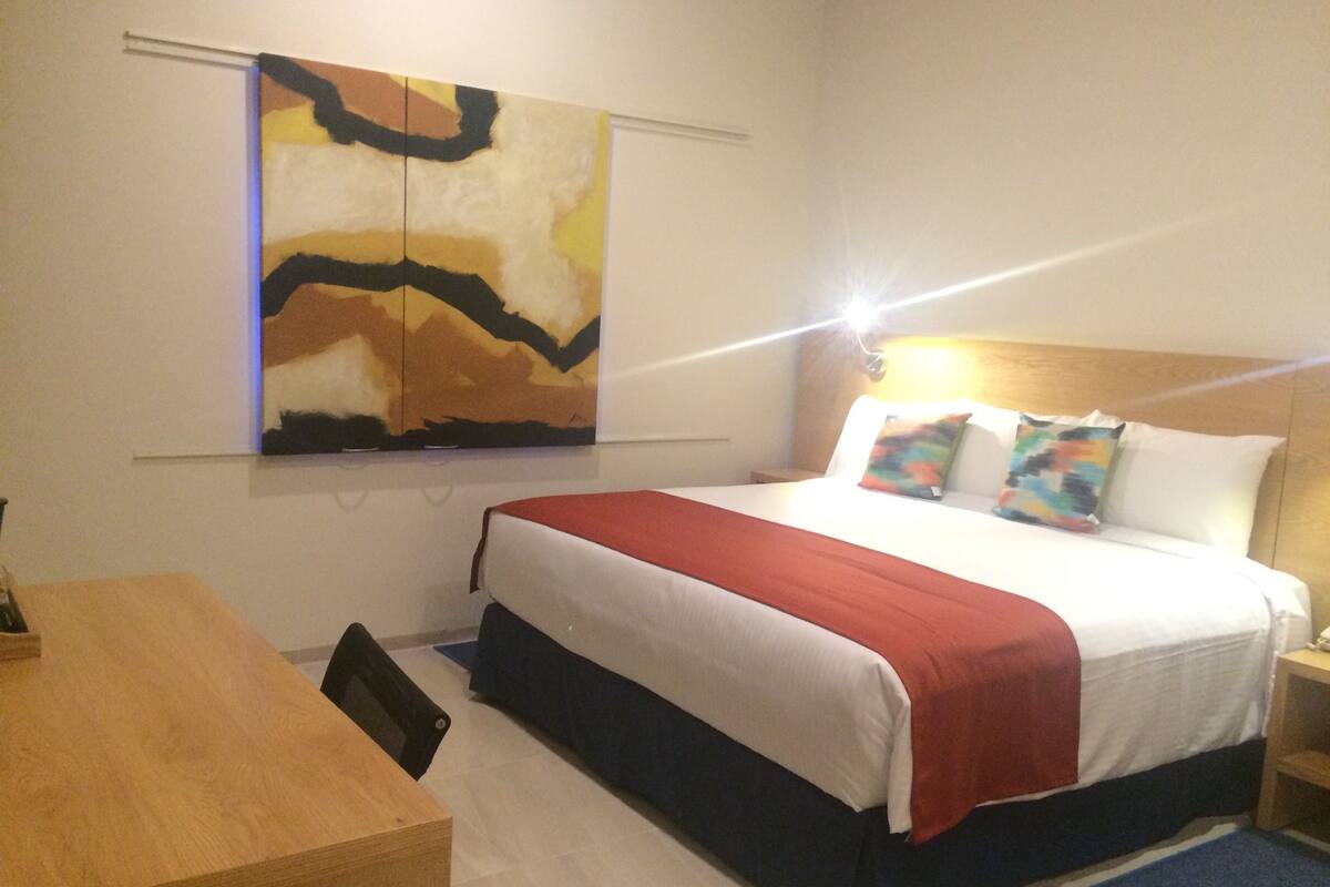 Une chambre d’hôtel avec un lit, un bureau et un grand tableau abstrait accroché au mur.