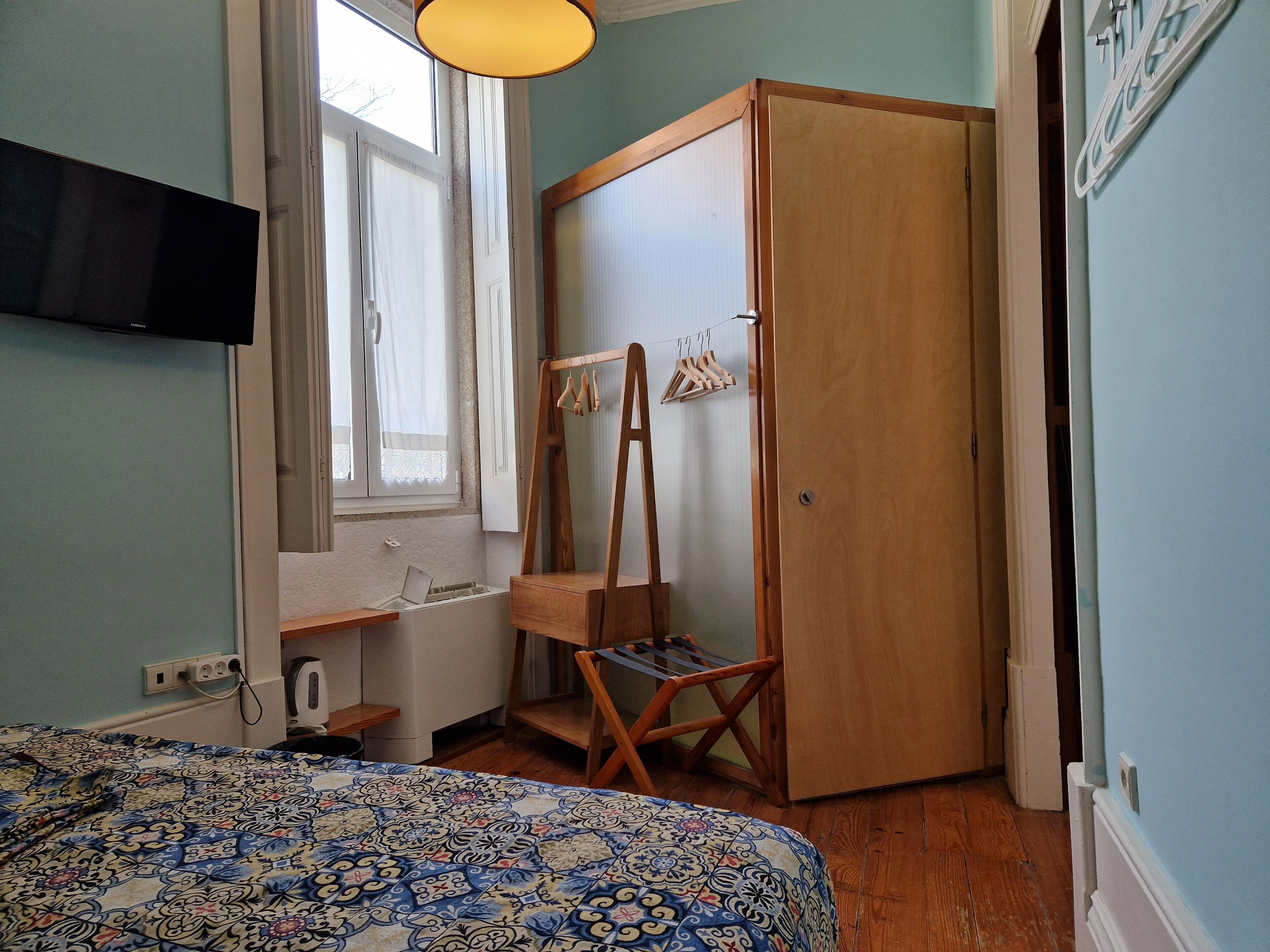 Ein Schlafzimmer mit Bett, einem Holzschrank, einem Schreibtisch mit Stuhl, einem Fenster mit Vorhängen und einer Kleiderstange.