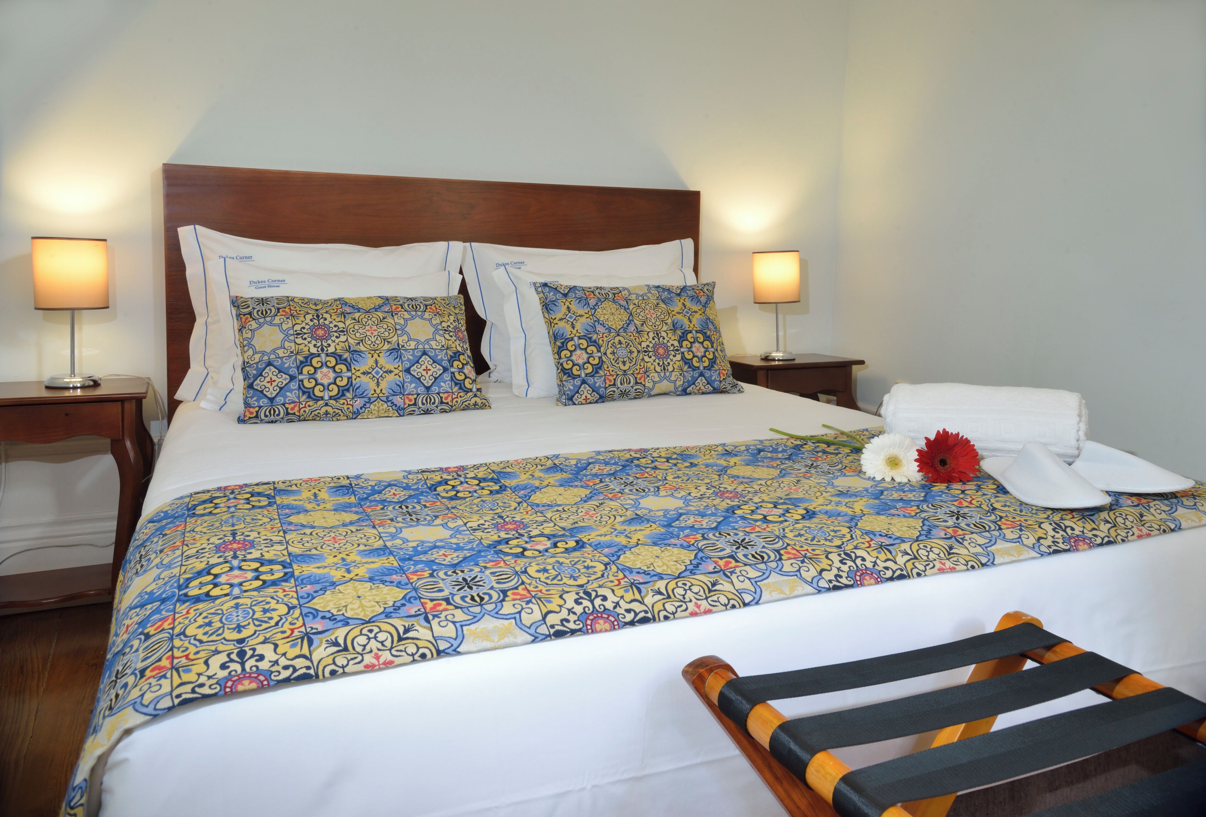 A neatly made bed with patterned bedding, two bedside tables with lamps, and a wooden chair.