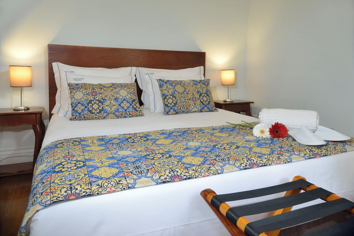A neatly made bed with patterned bedding, two bedside tables with lamps, and a wooden chair.
