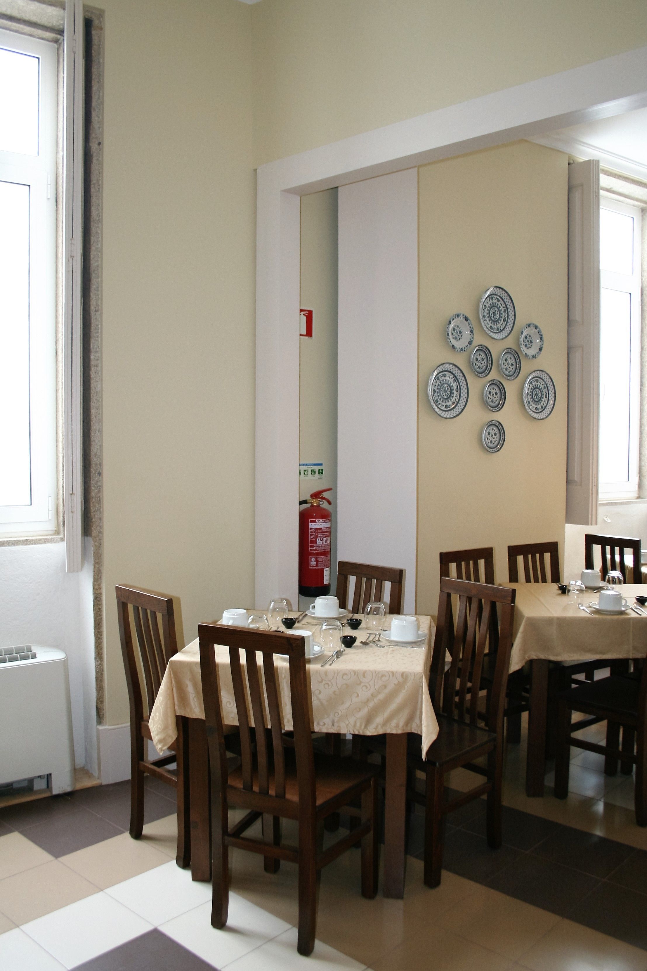 A dining area with tables set for four, wooden chairs, and a wall decorated with plates.