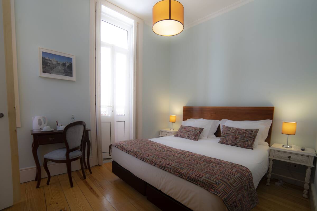 Ein ordentlich eingerichtetes Schlafzimmer mit Bett, Nachttischen, einem Sessel und einem Schreibtisch.