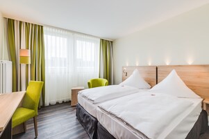 Una habitación de hotel con una cama, dos sillones, un escritorio y una lámpara.