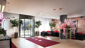 A modern lobby with a red carpet, potted plants, and a glass entrance.