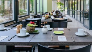 Un comedor con mesas dispuestas para el desayuno, incluyendo platos, tazas y cubiertos.