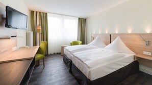 Habitación de hotel con cama, escritorio, silla, televisión y ventana con cortinas.