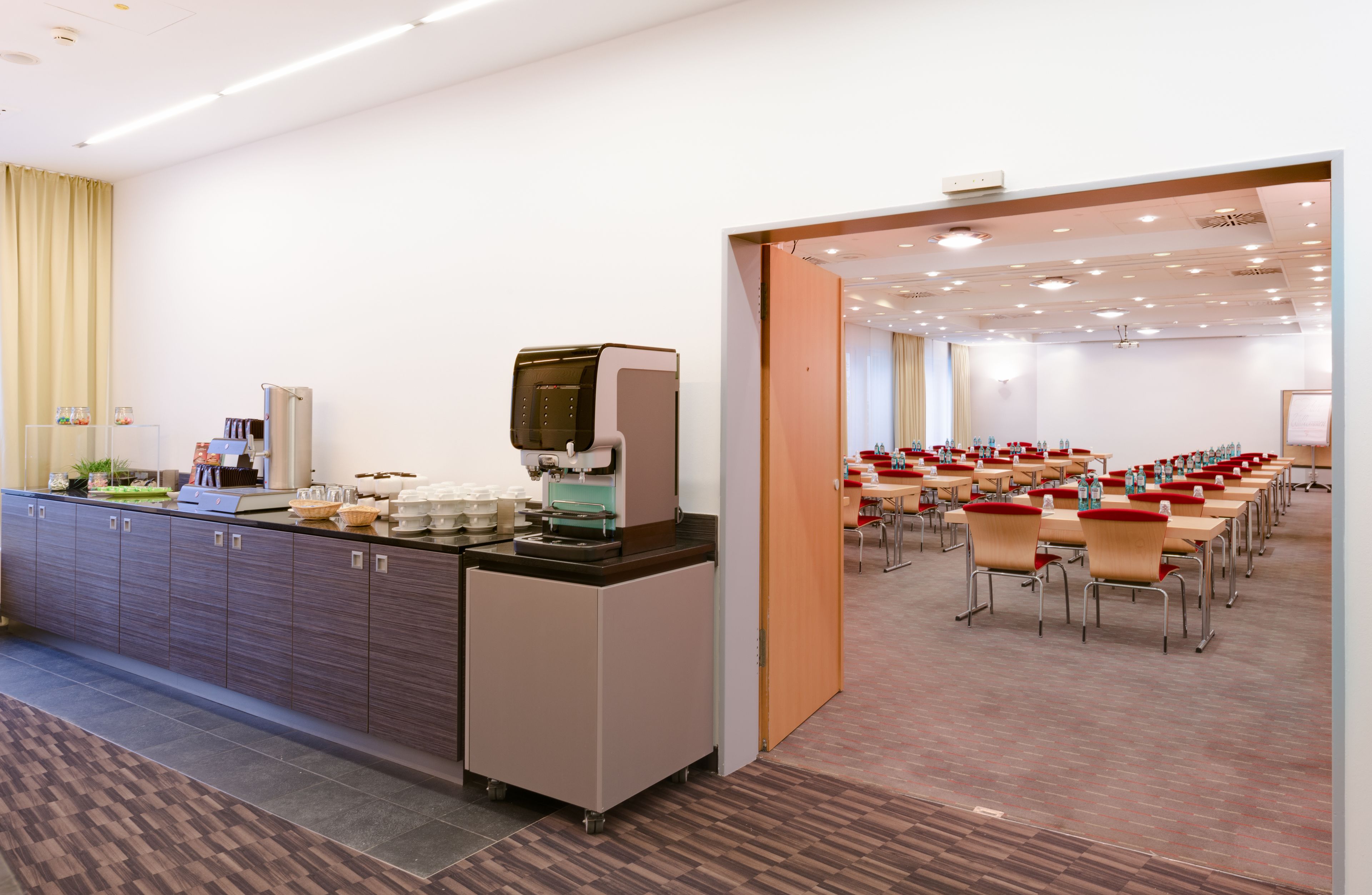 A conference room with rows of chairs and a buffet area with a coffee machine.