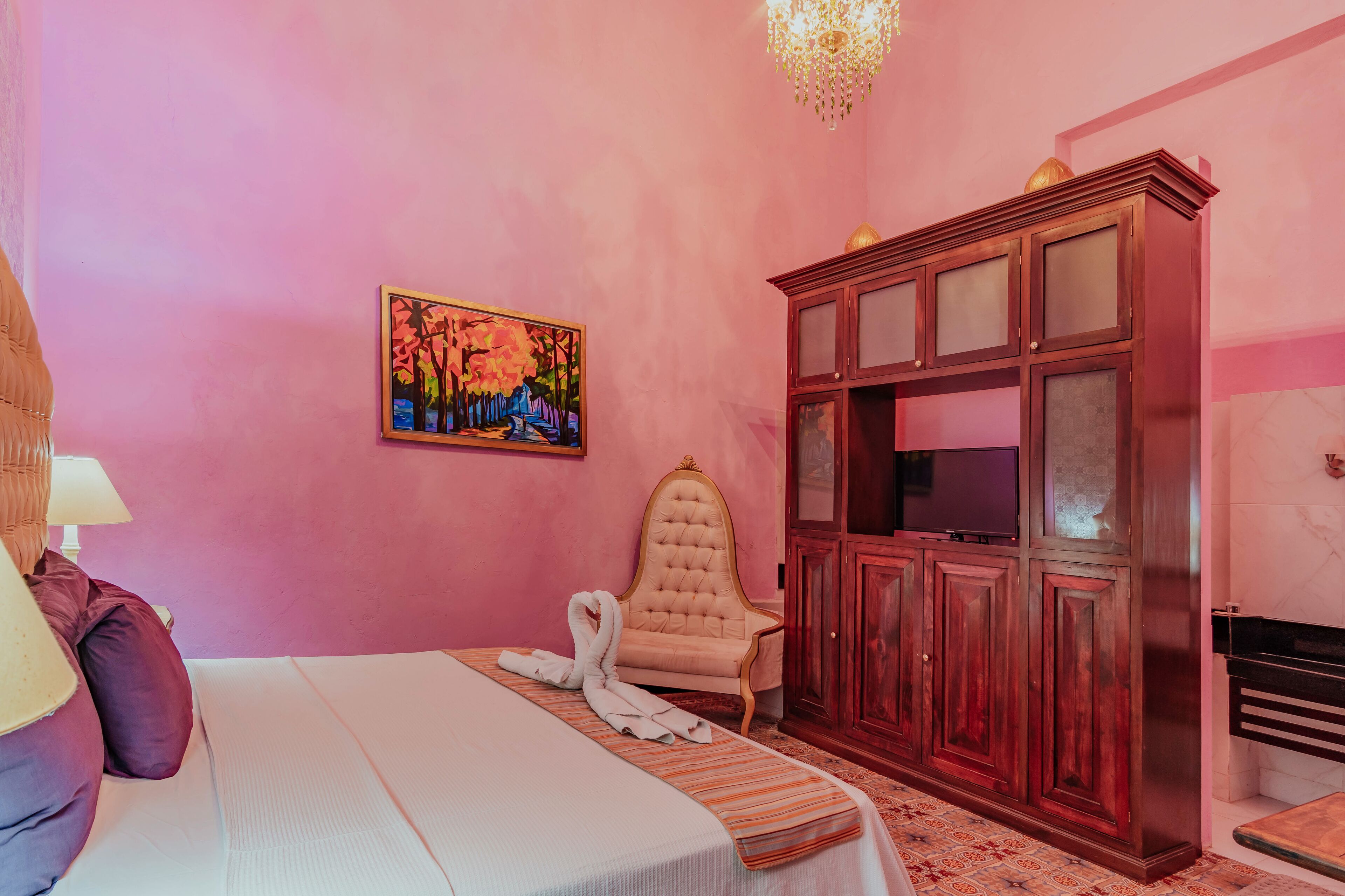 A room with a bed, a wooden cabinet, a painting, and a chandelier.