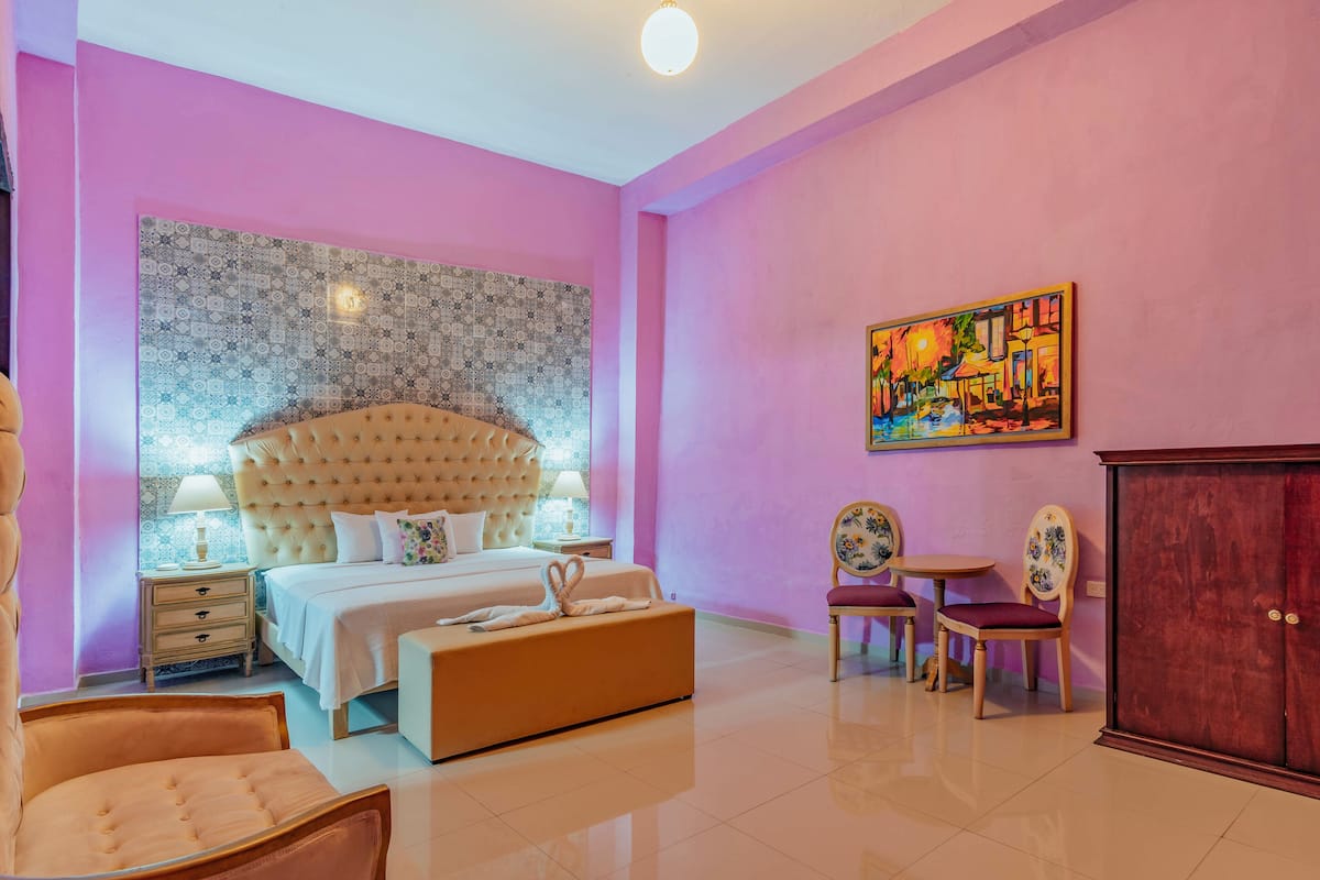 Quarto com cama grande, mesas de cabeceira, cadeira, mesa pequena e armário.