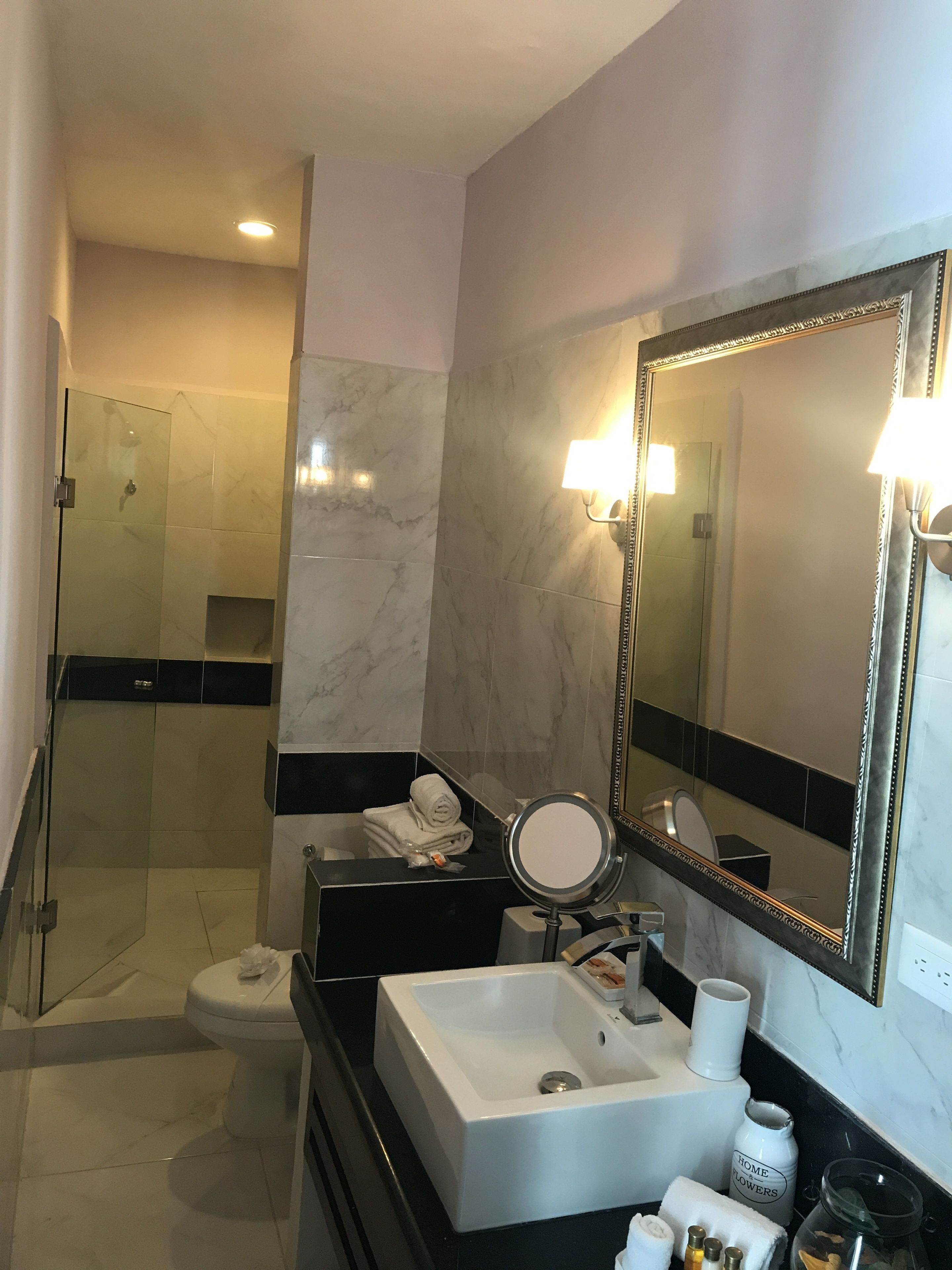 A modern bathroom with a glass shower enclosure, a white sink, a large mirror, and a black countertop.