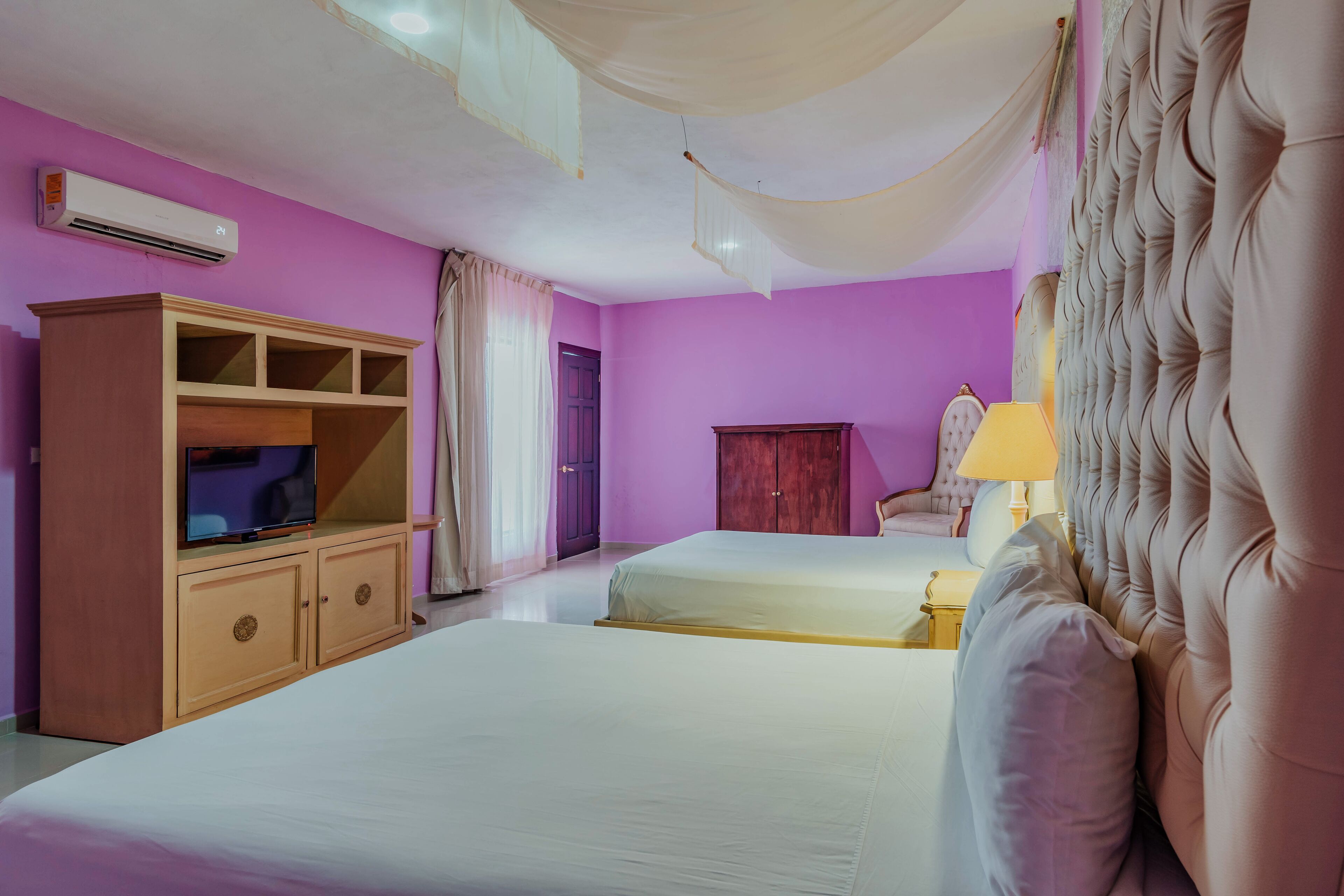 A hotel room with two beds, a television, a wardrobe, and a lamp.