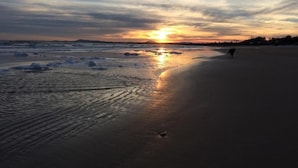 A beach at sunset with waves, a person walking, and a distant horizon. - Hostel Punta Ballena Bar (Punta Ballena)